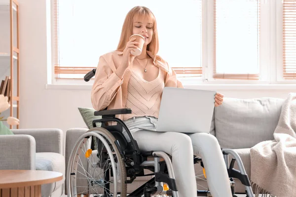 stock image Young woman in wheelchair with laptop drinking coffee at home