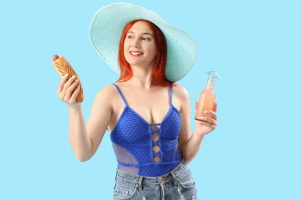 Beautiful young woman with french hot dog and lemonade on blue background