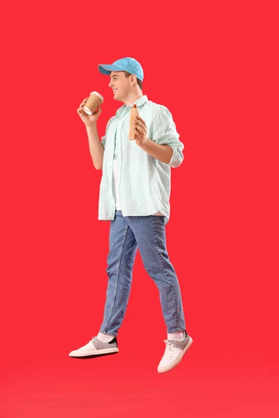 Прыгающий Молодой Человек Вкусным Хот Догом Чашкой Кофе Красном Фоне — стоковое фото