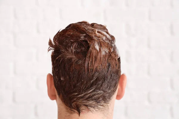 白レンガの背景 バックビューに対して髪にシャンプーを塗った若い男 — ストック写真