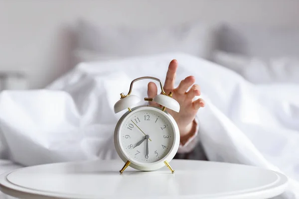 寝室の目覚まし時計のために到達する毛布の下の女性の手 — ストック写真
