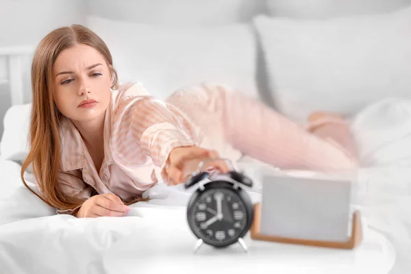Young woman on bed reaching for alarm clock in bedroom