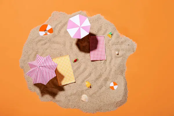 Creative summer composition with mini umbrellas, beach accessories and sand on orange background