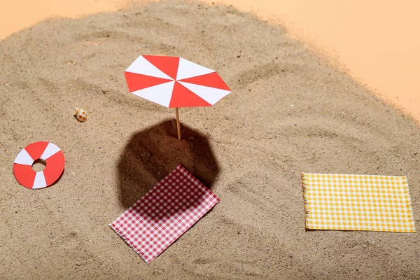 Creative summer composition with mini umbrella, beach accessories and sand on beige background