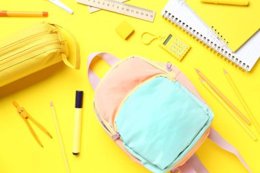 Sarı arka planda farklı kırtasiye malzemelerinin bulunduğu şık bir okul çantası ve kalem çantası.