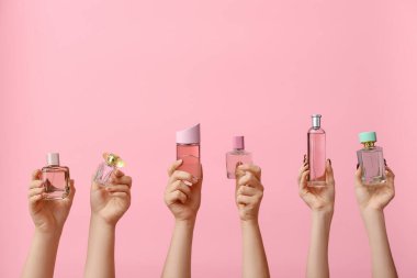Pembe arka planda farklı parfümler tutan kadın eller.