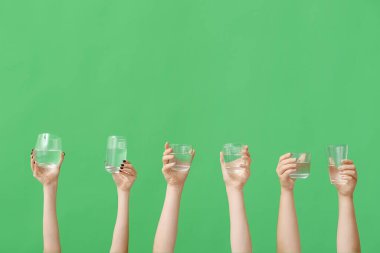Yeşil arka planda su bardakları tutan kadın eller.