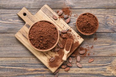 Bowls with cocoa powder and beans on wooden background clipart