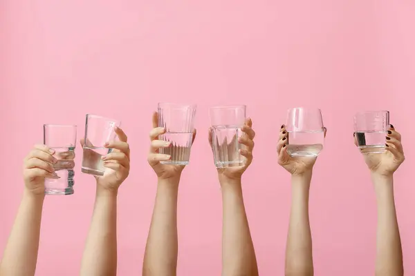 Mãos Femininas Segurando Copos Água Fundo Rosa — Fotografia de Stock