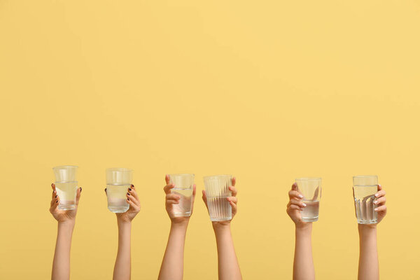 Female hands holding glasses of water on yellow background