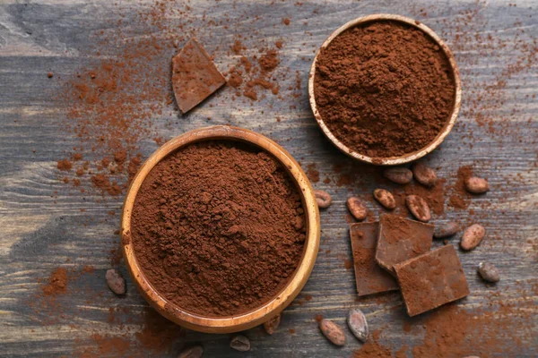 stock image Bowls with cocoa powder, beans and chocolate on wooden background