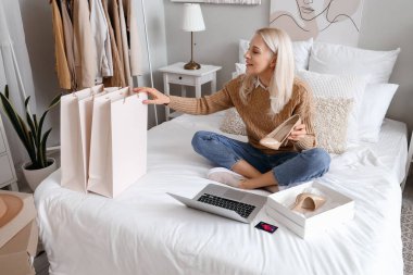 Dizüstü bilgisayarı olan ve yatak odasında yeni şeyler alan olgun bir kadın. İnternetten alışveriş