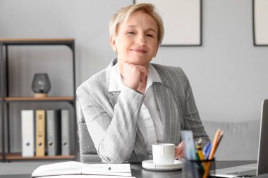 Olgun bir iş kadını ofiste kahve içiyor.