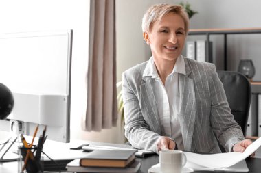 Olgun bir iş kadını ofiste belgelerle çalışıyor.