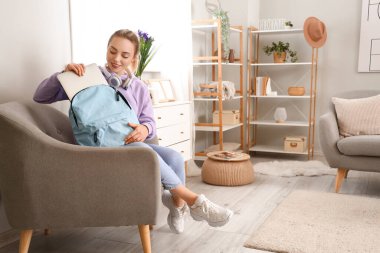 Bayan öğrenci evde sırt çantasından laptop alıyor.