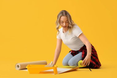 Sarı arka planda duvar kağıdı ölçen genç bir kadın.