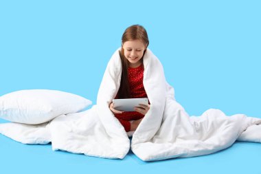 Mavi arka planda battaniye ve tablet bilgisayarı olan küçük bir kız.