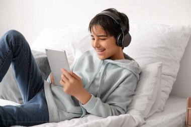 Kulaklıklı küçük çocuk yatak odasında tablet bilgisayar kullanıyor.