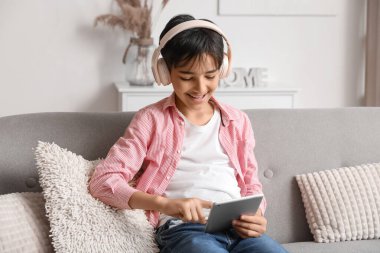 Kulaklıklı küçük çocuk evde tablet bilgisayar kullanıyor.