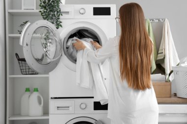 Çamaşır odasındaki çamaşır makinesine kirli çamaşır koyan kadın.