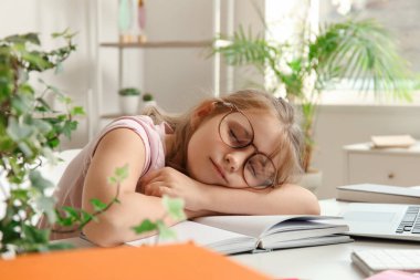 Evde ders çalışmaktan yorgun düşmüş küçük kız uyuyor.