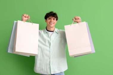 Yeşil arka planda alışveriş torbaları olan genç bir adam.
