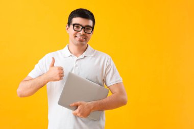 Dizüstü bilgisayarı olan erkek programcı sarı arka planda başparmağını kaldırıyor