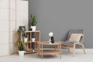 Açık ahşap sehpa, raf ünitesi ve gri duvarın yanındaki koltuk.