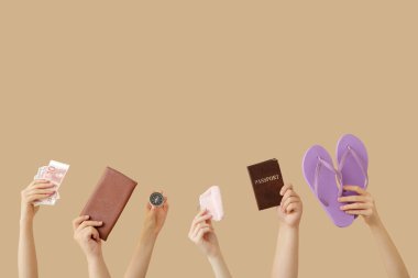 Pasaportu, parmak arası terlikleri, parası ve bej arka planda pusulası olan kadın elleri. Seyahat kavramı