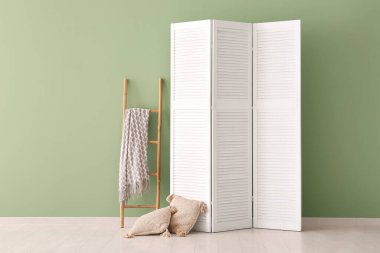 Katlanan ekran, merdiven ve yastıklar yeşil duvarın yanında