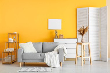 Modern oturma odası. Katlanan ekran, gri kanepe ve çekmeceler.