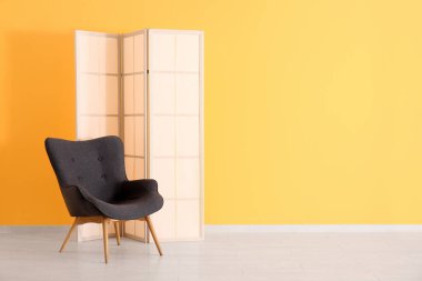 Turuncu duvarın yanında gri koltuk ve katlanır ekran