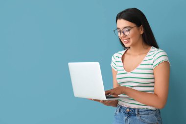 Mavi arka planda dizüstü bilgisayarla çalışan mutlu kadın programcı.