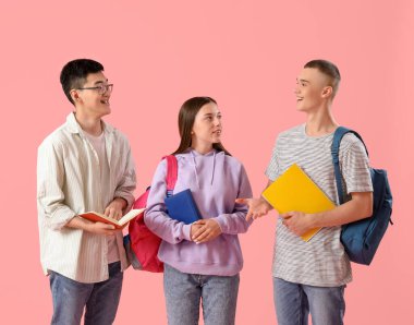 Sırt çantaları ve pembe arka planda not defterleri olan mutlu öğrenciler