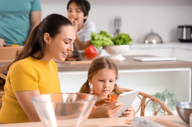 Tablet bilgisayarlı küçük bir kız ve annesi mutfakta.