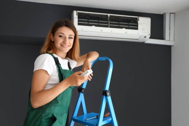 Kadın teknisyen odada klimayı açıyor.