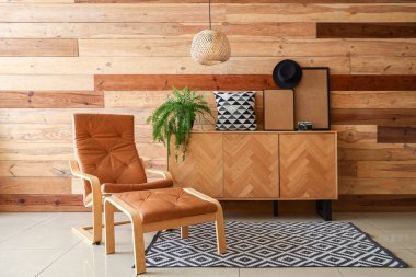 Tahta duvarın yanında taburesi ve büfesi olan kahverengi koltuk.