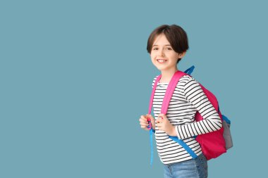 Mavi arka planda sırt çantası olan mutlu küçük çocuk.