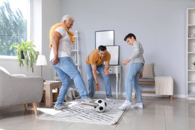 Babası ve dedesiyle evde futbol oynayan küçük bir çocuk.