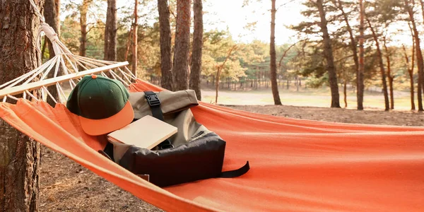 Hammock with bag, hat and book in forest on summer day