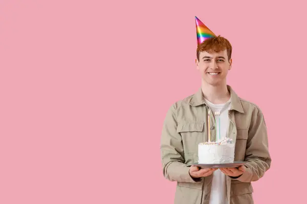 Young man with birthday cake on pink background