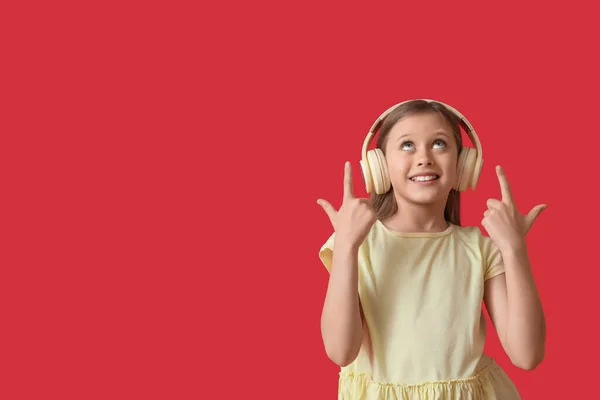 Kulaklıklı Küçük Kız Kırmızı Arka Plandaki Bir Şeyi Işaret Ediyor — Stok fotoğraf