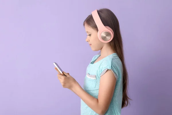 Kulaklıklı Küçük Kız Eflatun Arka Planda Cep Telefonu Kullanıyor — Stok fotoğraf