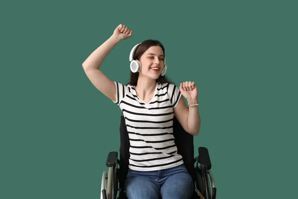 Young woman with headphones in wheelchair on green background