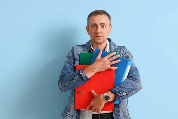 Stressed mature man with folders on blue background. Deadline concept