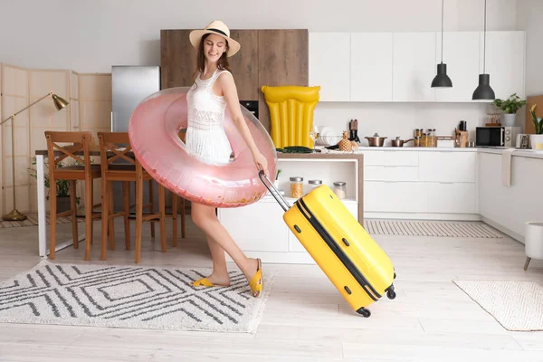 Young woman with swim ring and suitcase ready for summer vacation in kitchen
