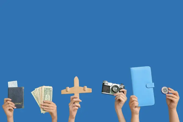 Female hands with passport, ticket, money, wooden airplane, photo camera and compass on blue background. Travel concept