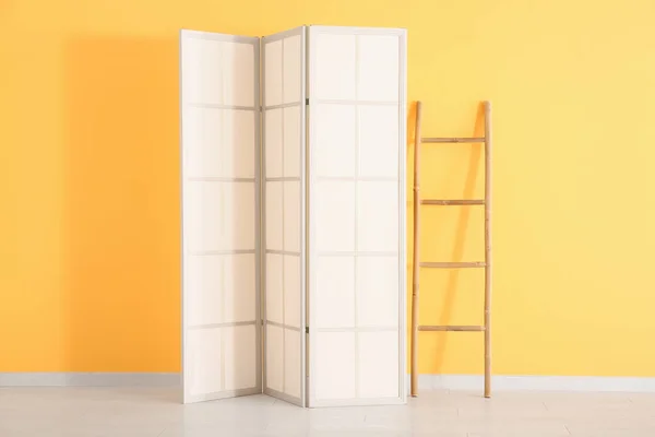 Folding screen and ladder near orange wall
