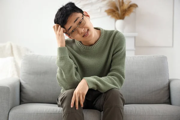 Upset young Asian man in earphones video chatting on sofa at home