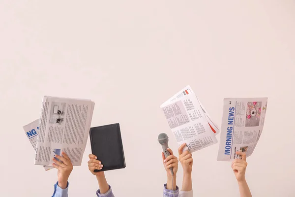 Female hands with different newspapers, notebook and microphone on light background